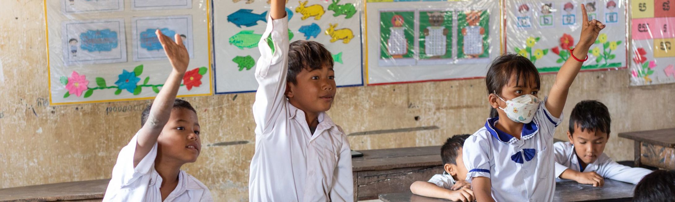 Room to Read Cambodian students eagerly raising their hands in class.