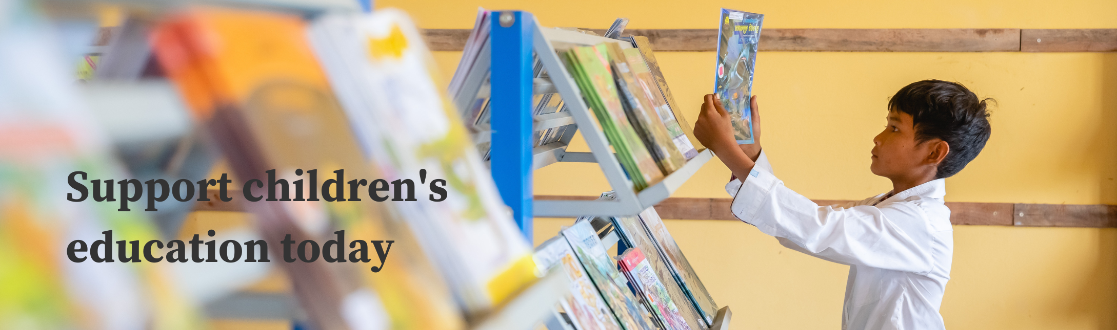 Young boy from Cambodia picking up a book from a library shelf
