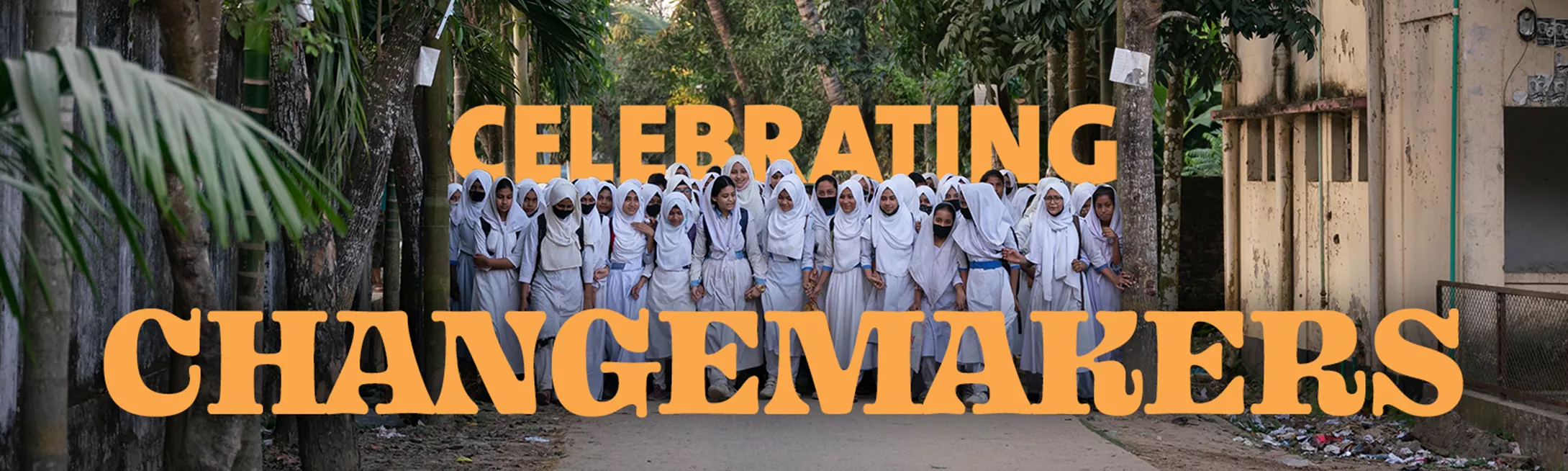 Big group of girls in Bangladesh dressed in white walking outside together surrounded by trees with the words "Celebrating Changemakers" overlaid