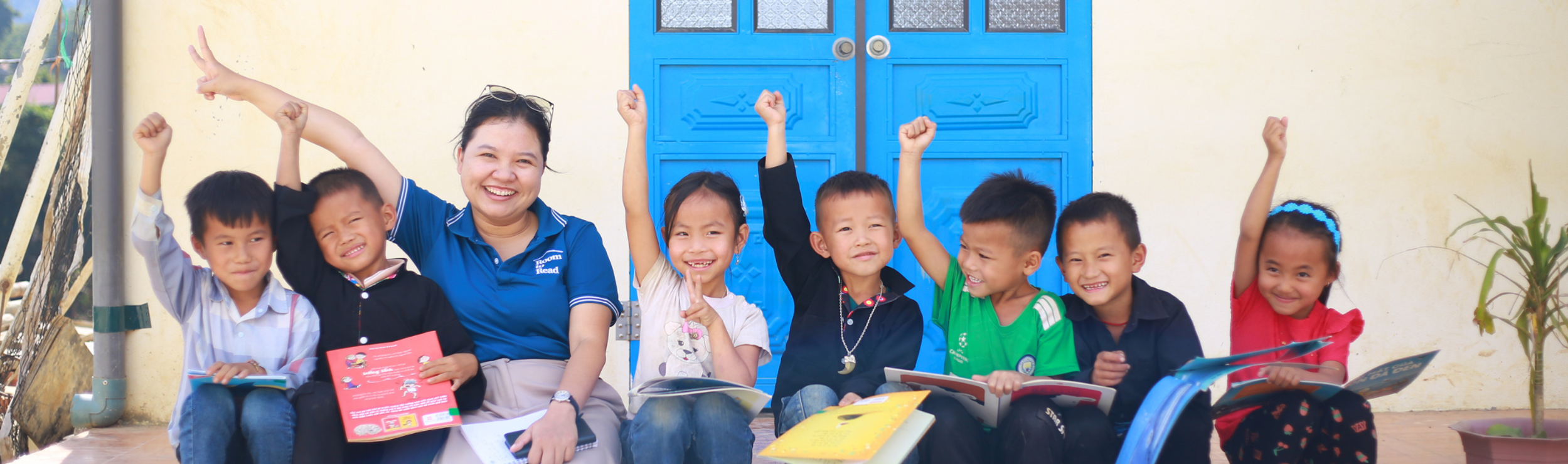 Promoting book use in a digital world outside a school library in Vietnam children hold books, smiling at the camera.