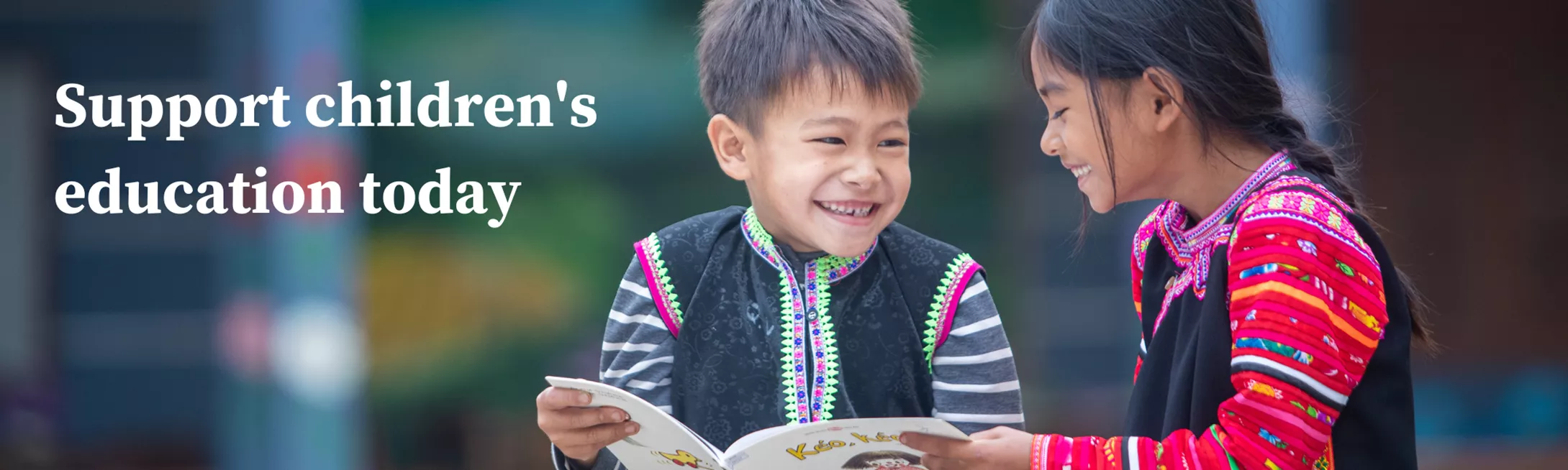 2 children in Cambodia laughing as they read a book with text overlay that says "Support children's education today"