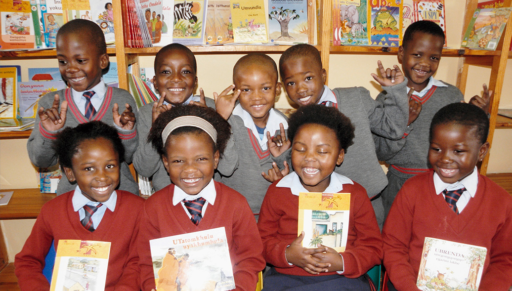 Nine South African students poses for photo in front of bookshelves. Five girls in the front are holding a book each.