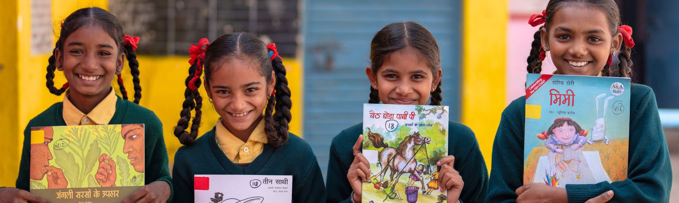4 Indian students are holding Room to Read books, smiling.