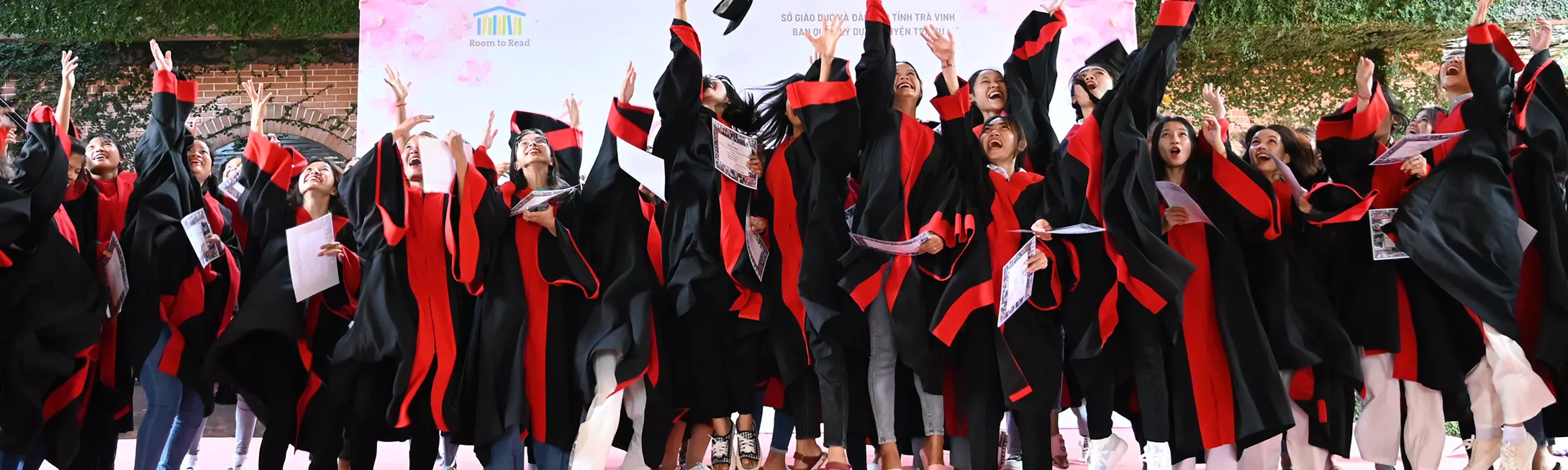 Group of Vietnamese girls in graduation robes throwing graduation caps in the air