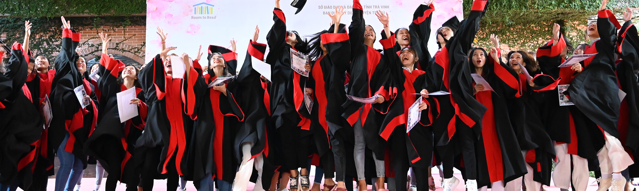 Group of Vietnamese girls in graduation robes throwing graduation caps in the air