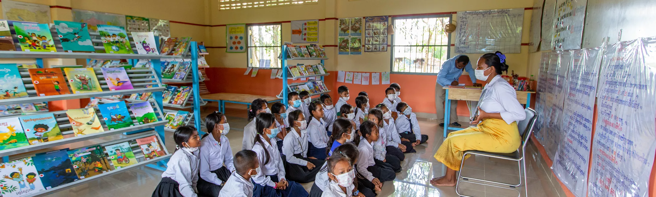 A teacher reads aloud to a group of primary school students in a school library in Cambodia