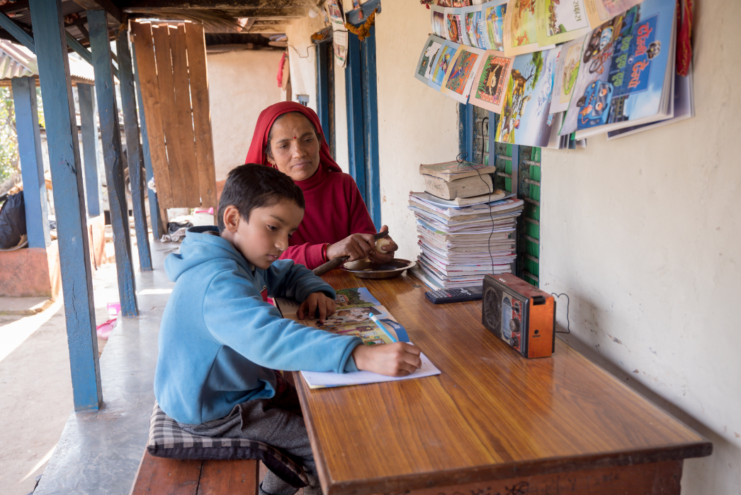 Boy and mother sitting at table outside with a big stack of books and books hanging on the wall