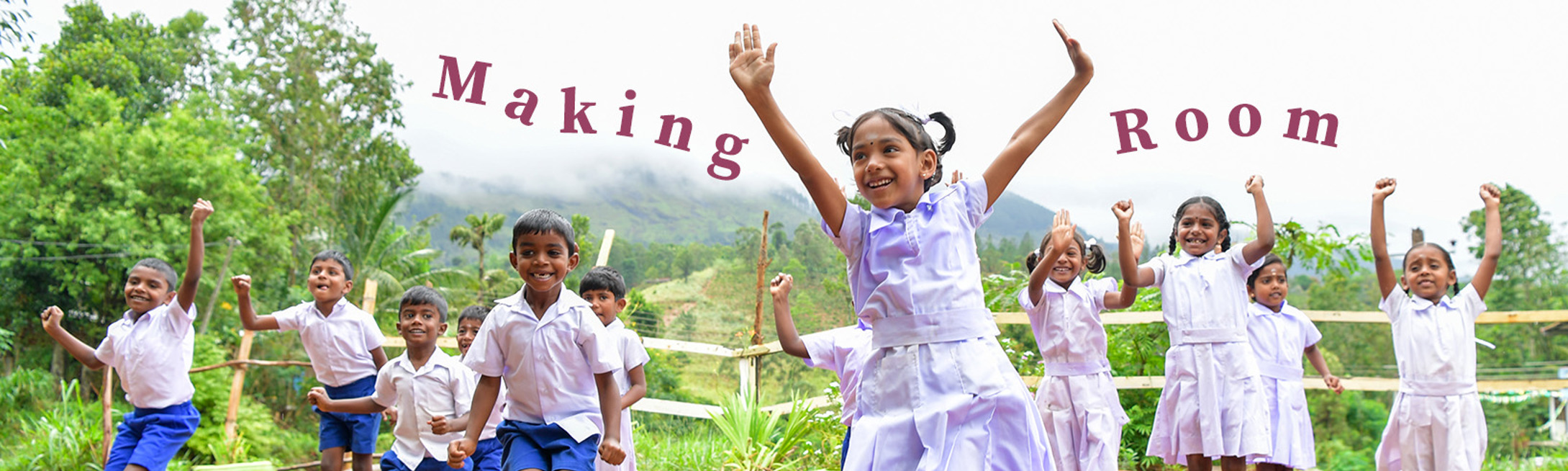 Big group of Sri Lankan elementary students jumping for joy outside, in front of a fenced greenery. The girls are wearing short-sleeve white shirts and white pleated skirts while boys are wearing the same shirts with blue shorts. Overlaid words read "Making Room"