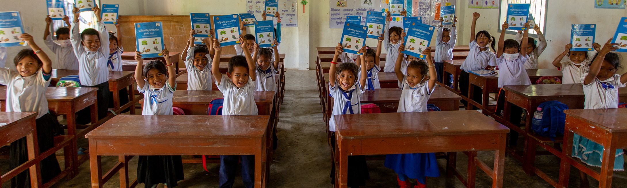 Students in classroom holding up books and smiling